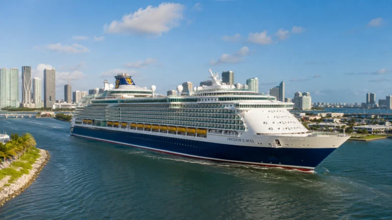 Cruise ship sailing past a high-rise waterfront under scattered clouds