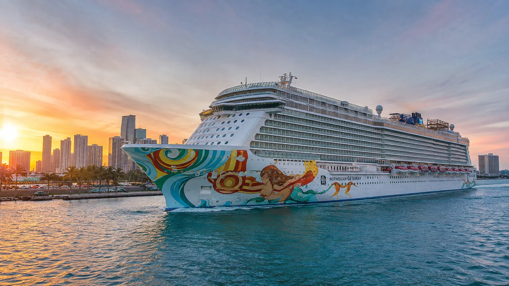 Norwegian Getaway sailing past a city skyline at sunset