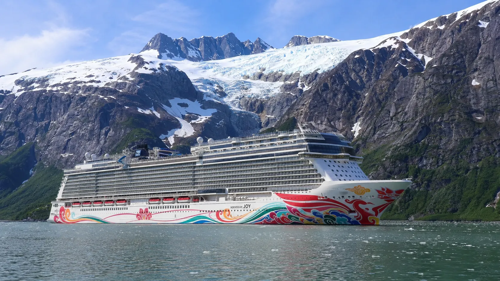 Cruise ship with colorful hull artwork beneath snowy mountain peaks