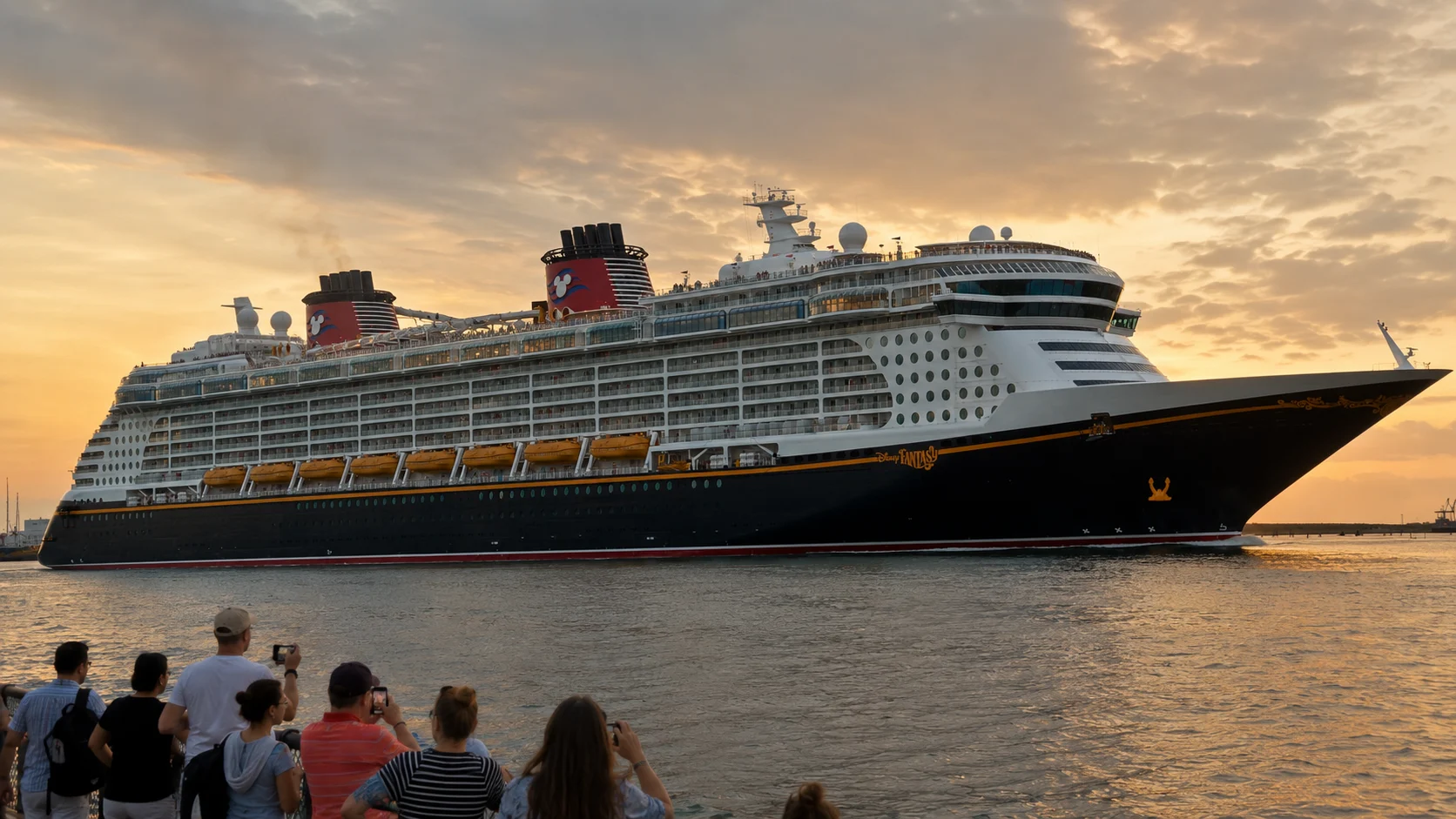 Disney cruise ship sailing past a waterfront at sunset