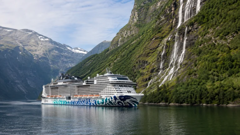MSC cruise ship sailing through a green fjord below a waterfall