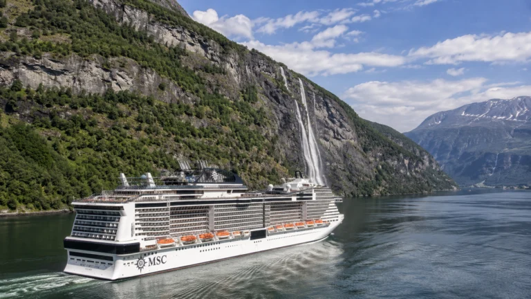 MSC cruise ship sailing through a steep fjord below a waterfall