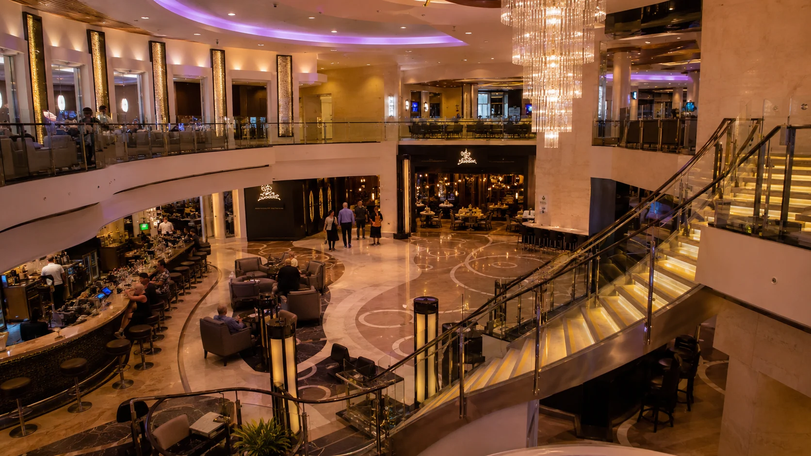 Multi-level cruise ship atrium with sweeping staircases and chandeliers