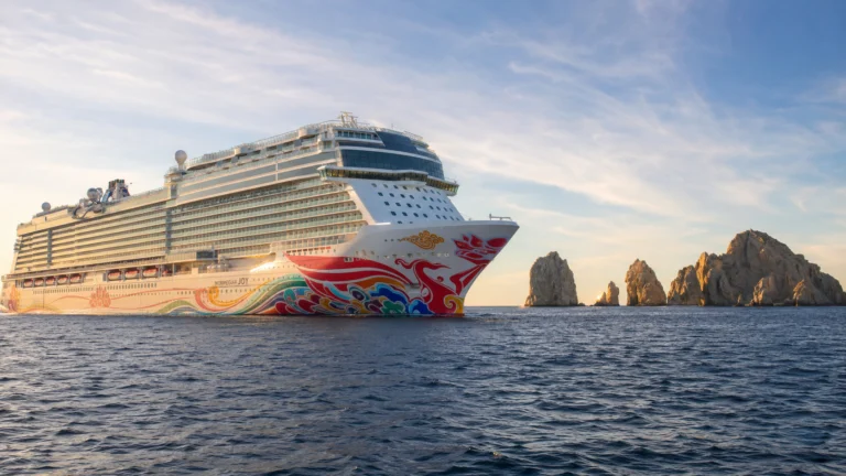 Cruise ship with colorful hull artwork sailing past rocky sea cliffs