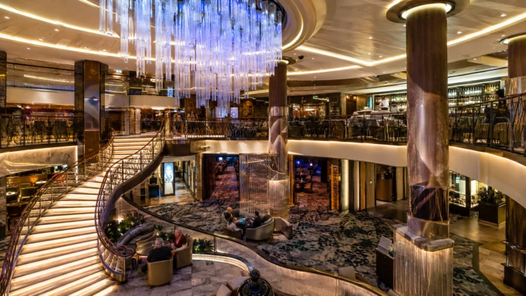 Multi-level cruise ship atrium with a sweeping staircase and crystal chandelier