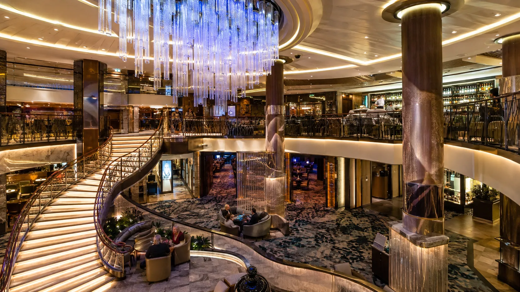 Multi-level cruise ship atrium with a sweeping staircase and crystal chandelier