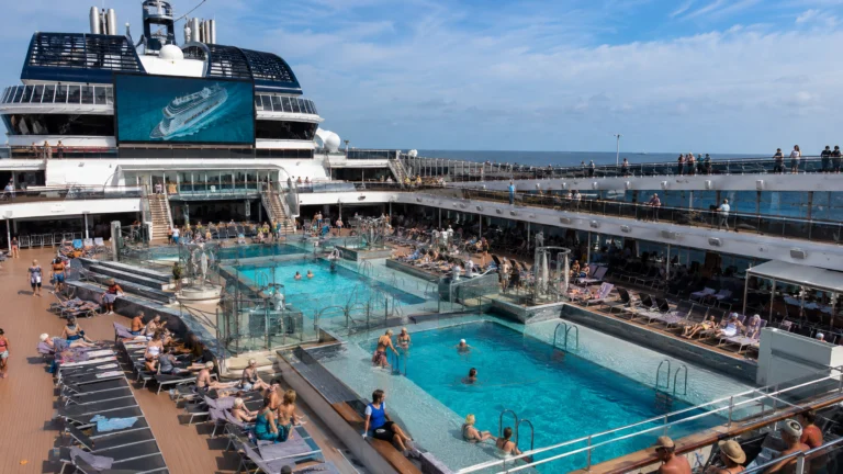 Busy cruise ship pool deck with swimmers and rows of loungers