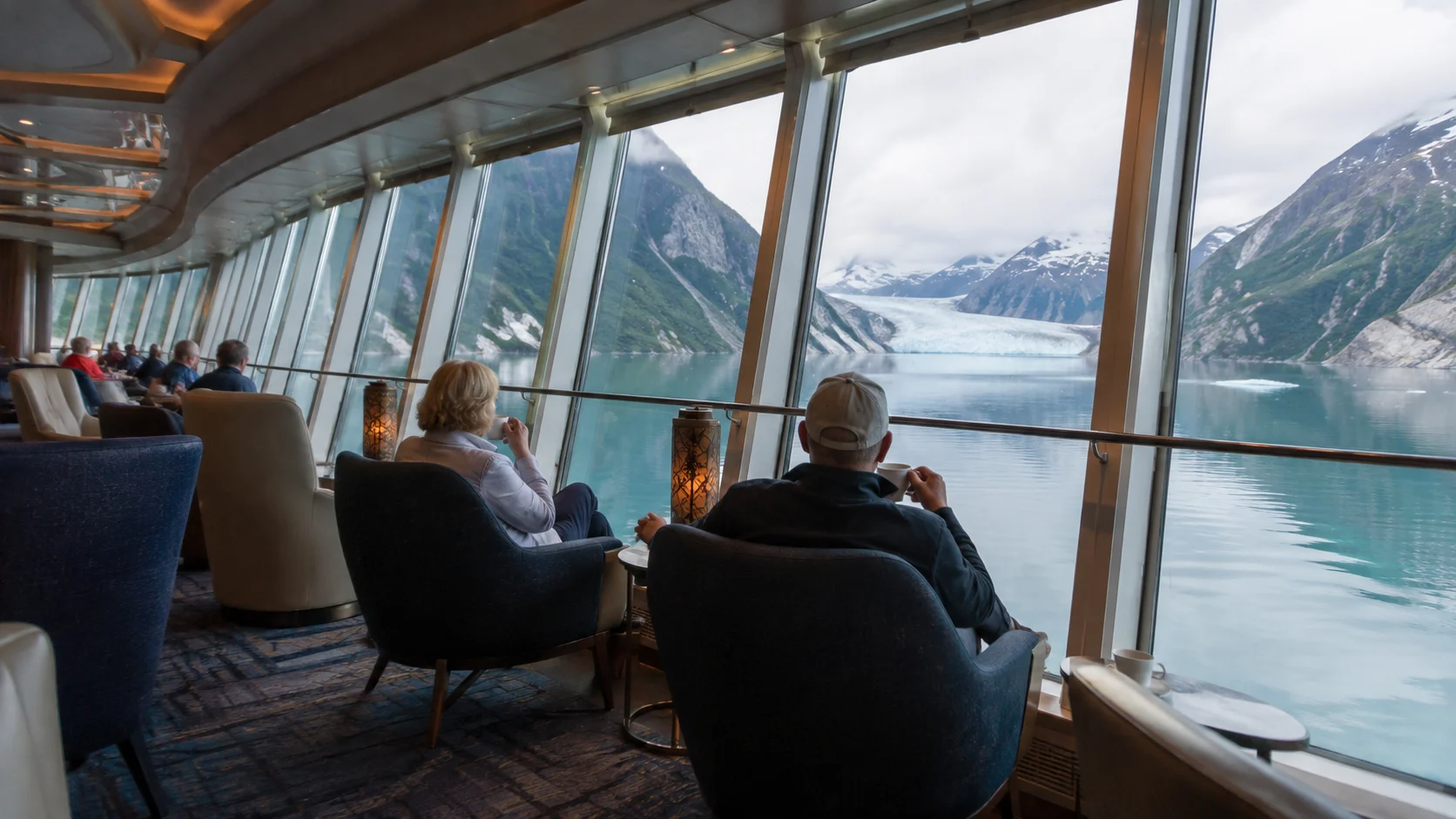 Passengers viewing a glacier and mountains from a panoramic lounge