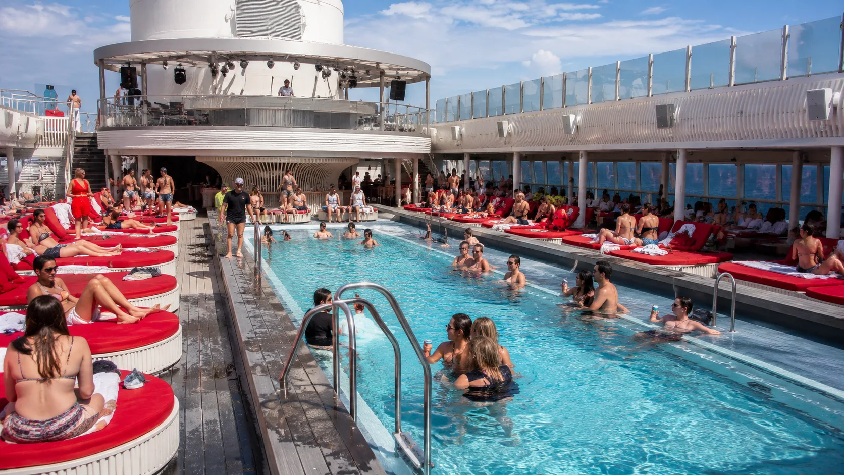 Passengers relaxing around a cruise ship pool with red loungers