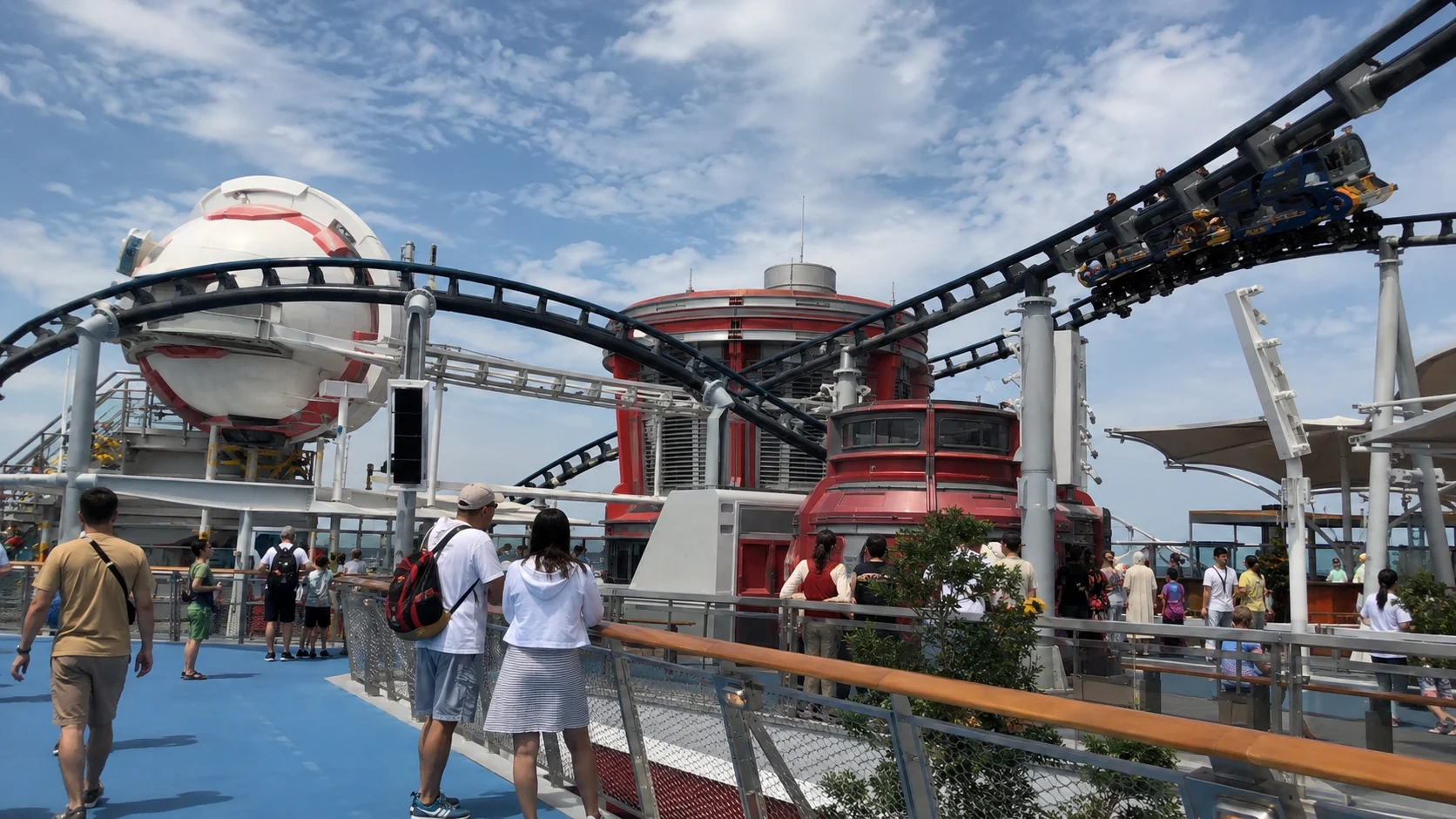 Passengers walking beneath an elevated ride track on a cruise ship deck