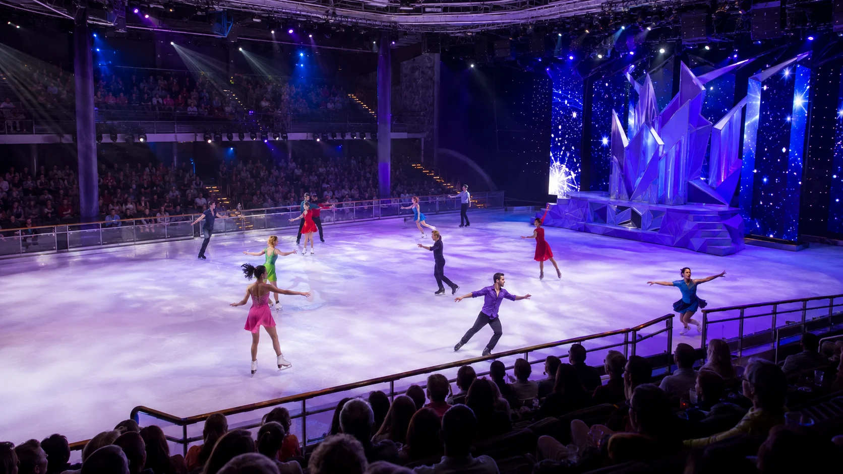 Figure skaters performing in a blue-lit cruise ship ice show