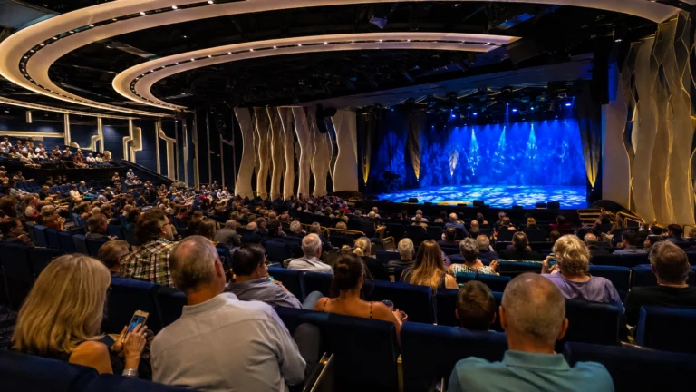 Packed cruise ship theater facing a blue-lit stage