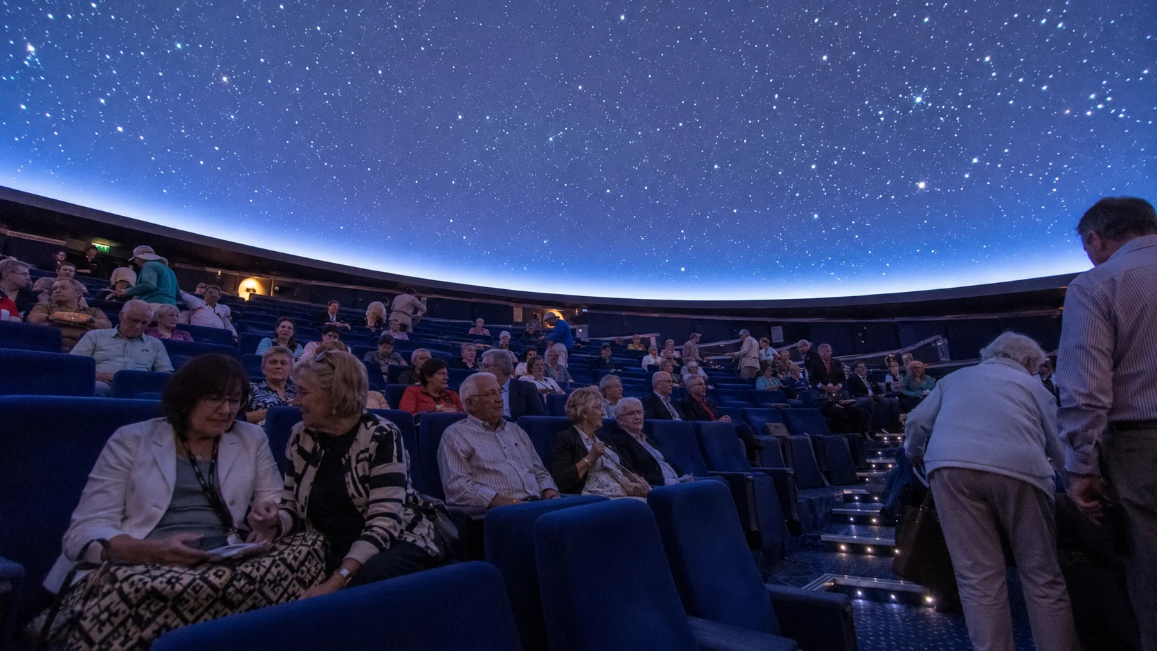 Passengers seated beneath a star-filled planetarium dome