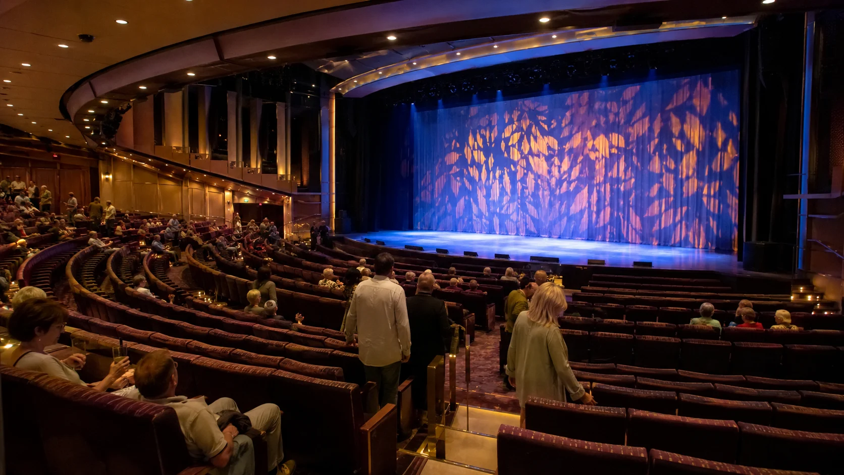 Audience seated in a cruise ship theater with a colorful stage