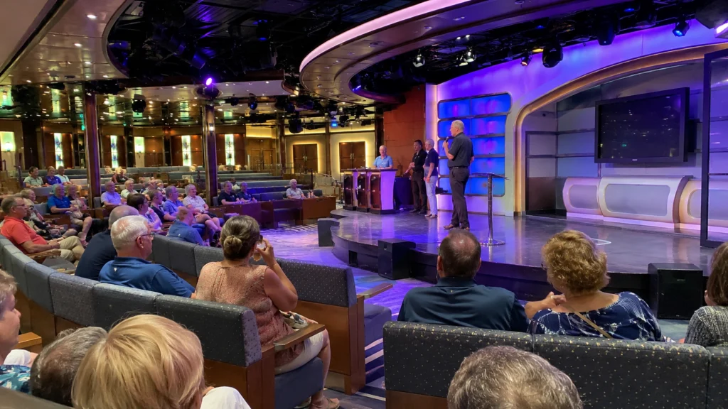 Audience watching a presentation in a purple-lit cruise ship studio