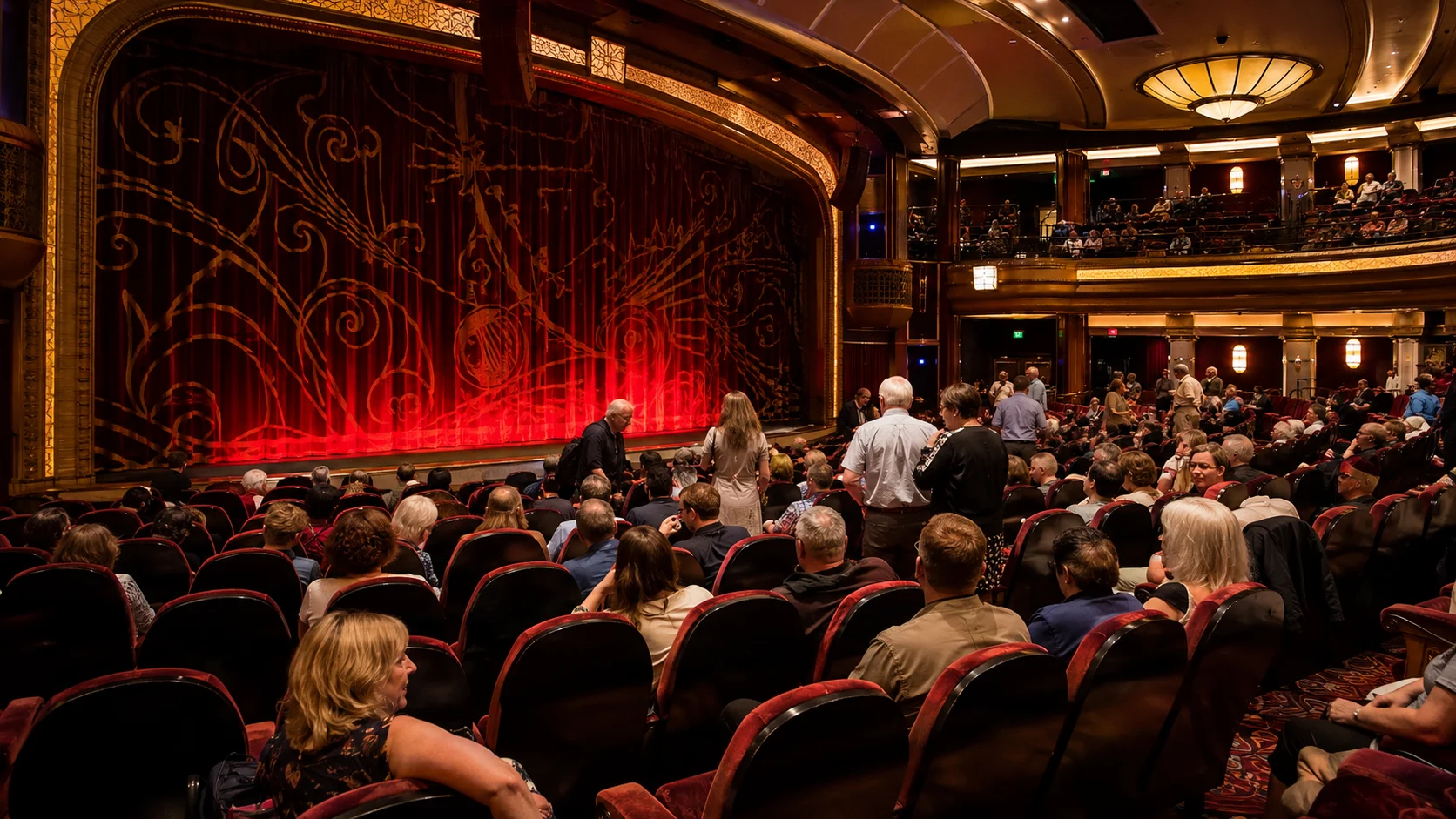 Audience seated before a red-curtained theater stage