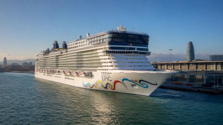 Cruise ship with colorful hull artwork docked near a waterfront tower
