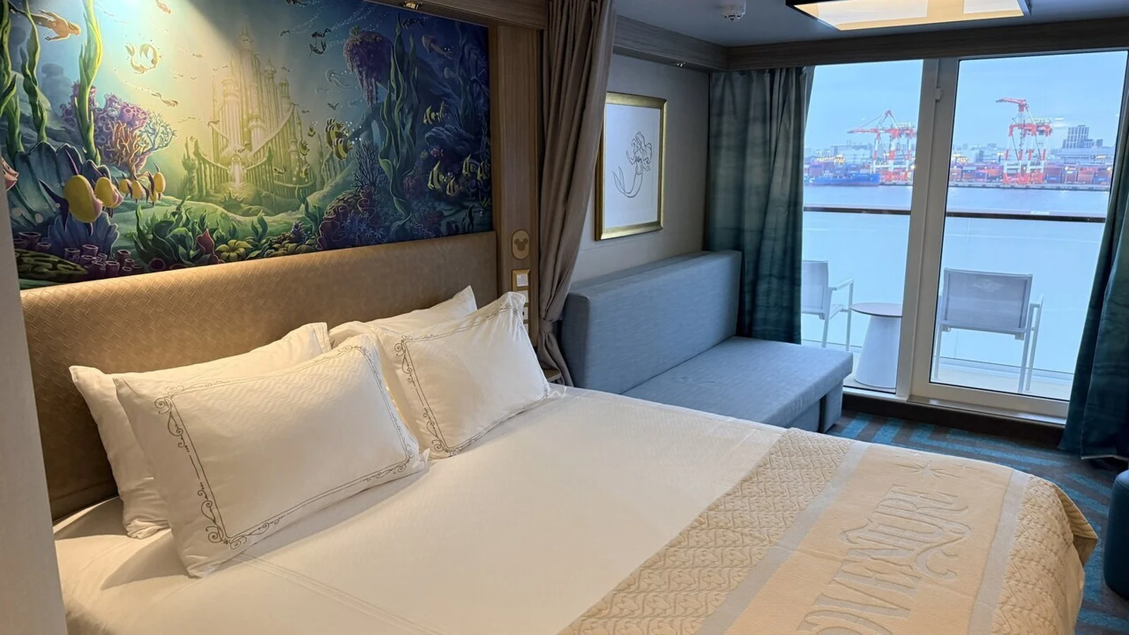 Cruise cabin with a double bed, underwater mural, sofa, and balcony