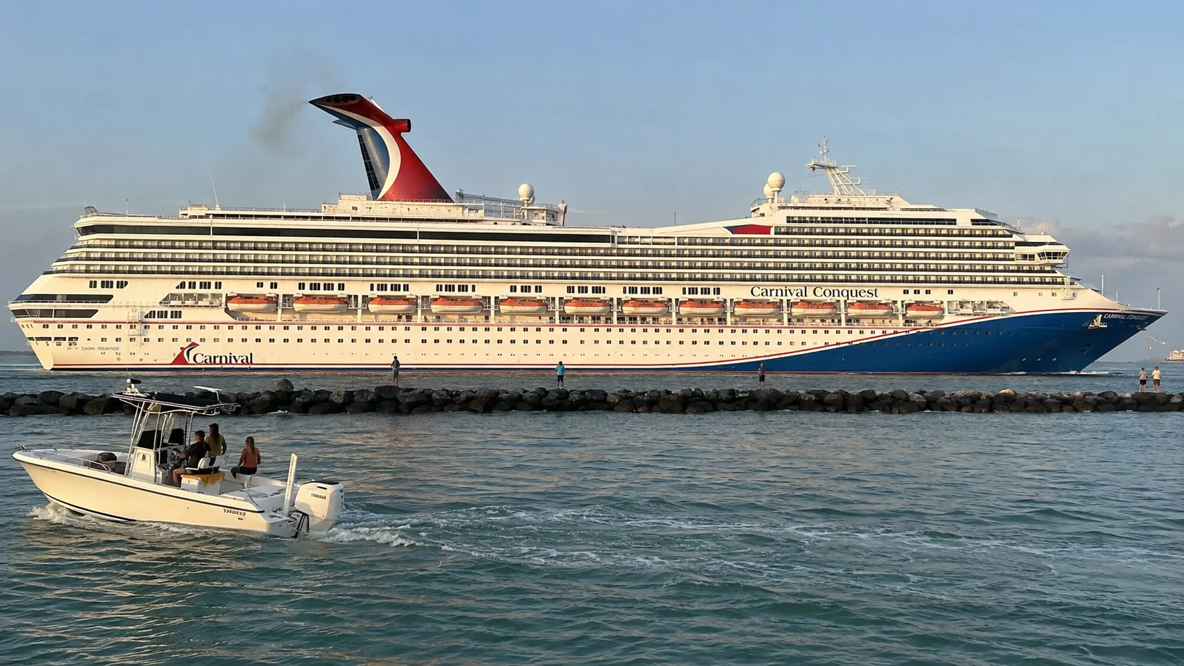 Carnival cruise ship passing a breakwater with a small boat in the foreground