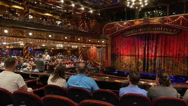 Audience seated before a red curtain in an ornate cruise ship theater