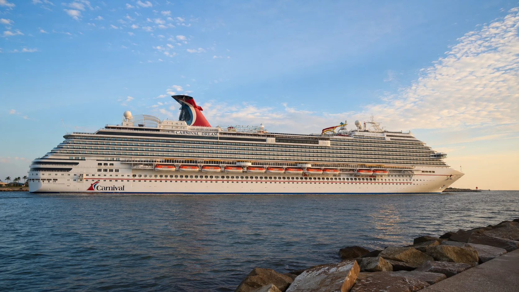 Carnival cruise ship sailing past a rocky breakwater