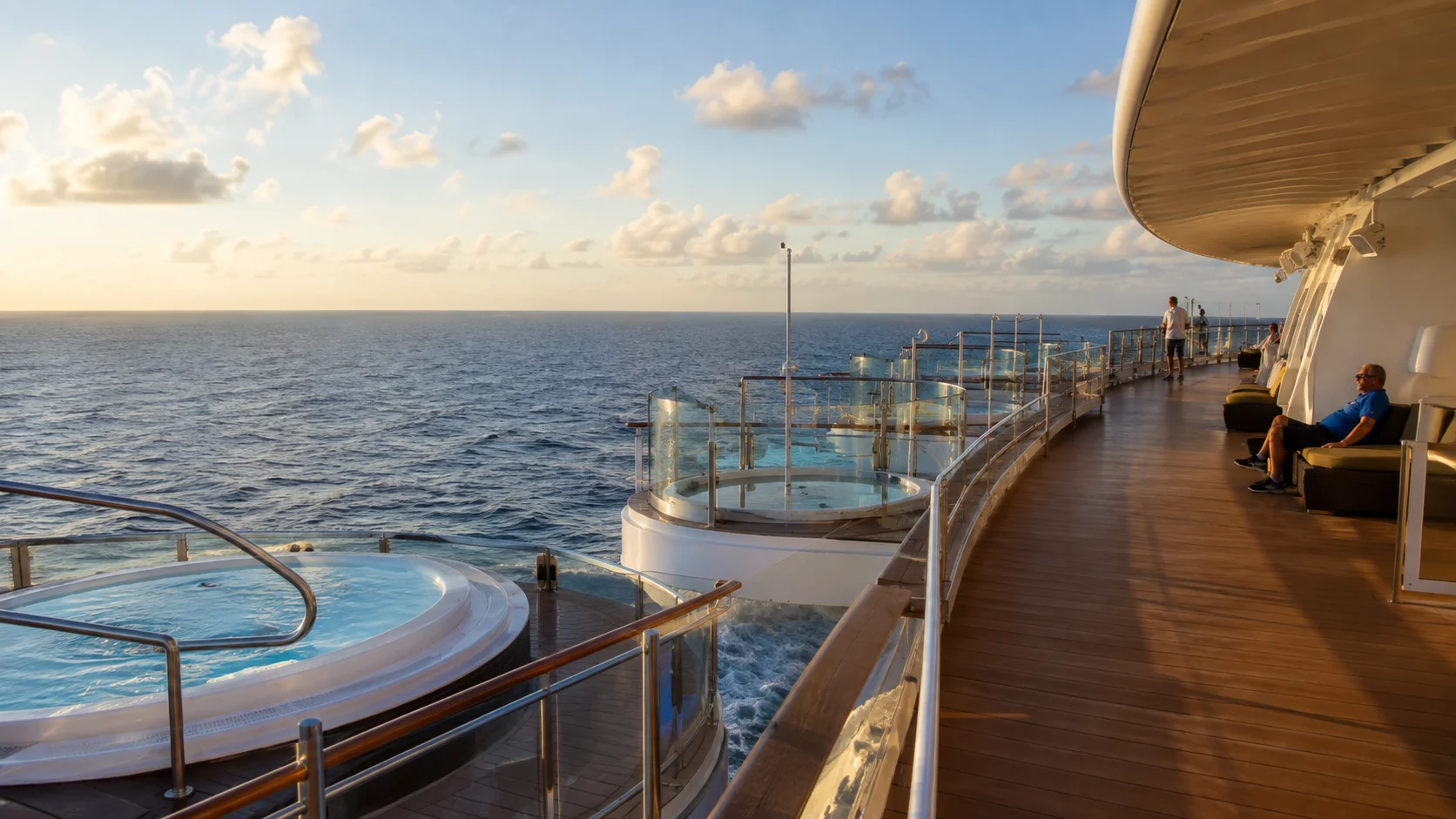 Ocean-facing hot tubs beside a curved cruise ship promenade at sunset