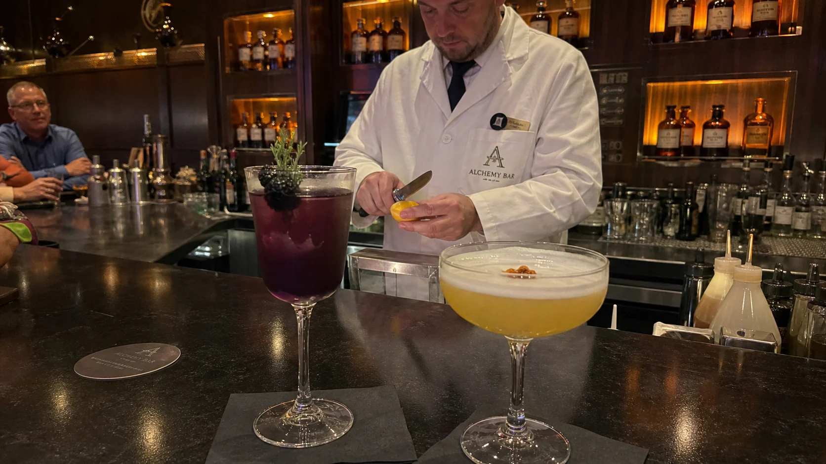 Bartender preparing garnishes beside two cocktails