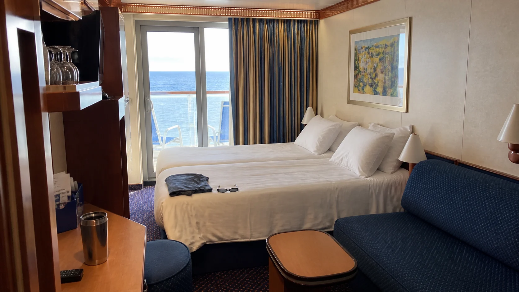 Cruise cabin with a double bed, blue sofa, and glass balcony doors