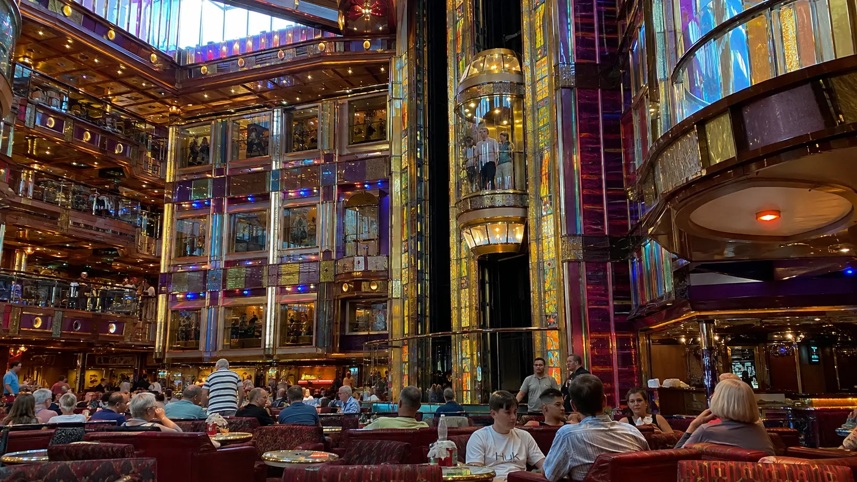 Passengers seated in a colorful multilevel atrium with glass elevators