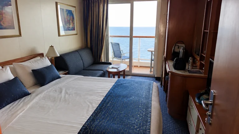 Cruise cabin with a double bed, blue cushions, sofa, and balcony