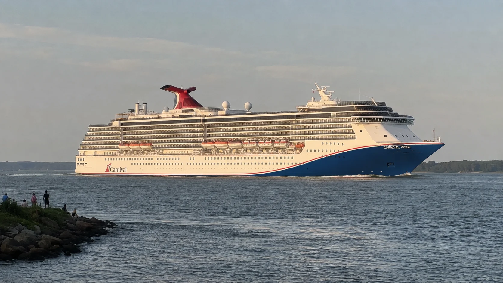 Carnival cruise ship sailing past a shoreline at dusk