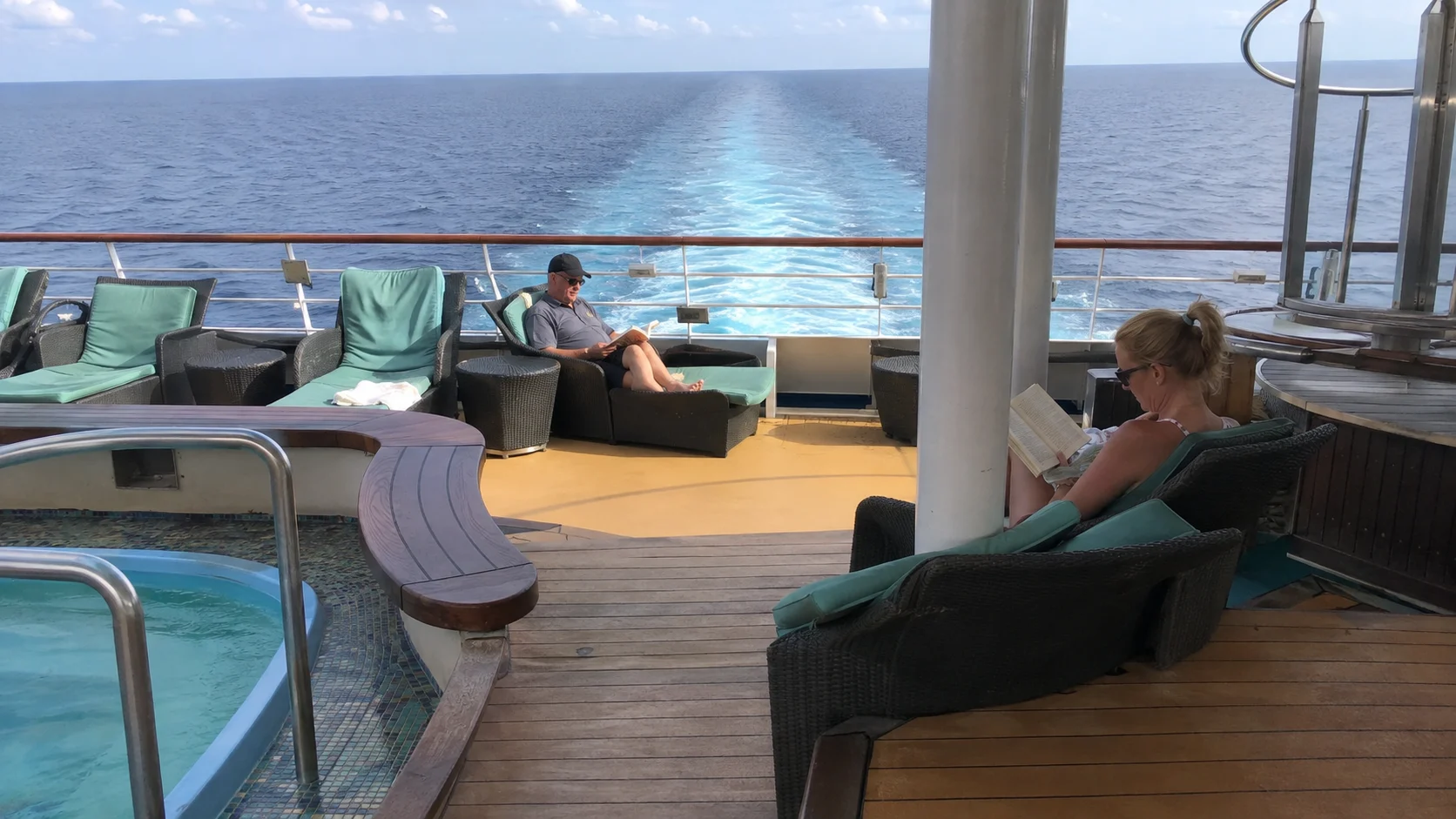 Passengers relaxing beside an aft-deck hot tub overlooking the ship's wake
