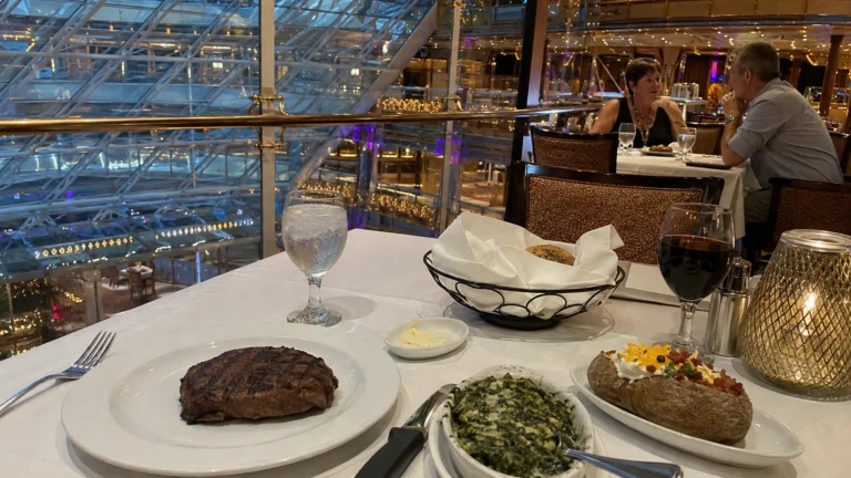 Steak, baked potato, and spinach at a restaurant overlooking a ship's atrium