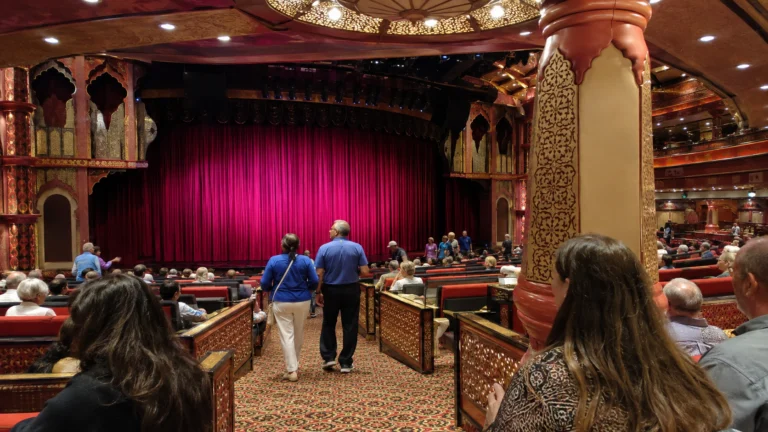 Passengers entering a theater with a red stage curtain