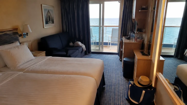 Cruise cabin with twin beds, blue sofa, and balcony doors