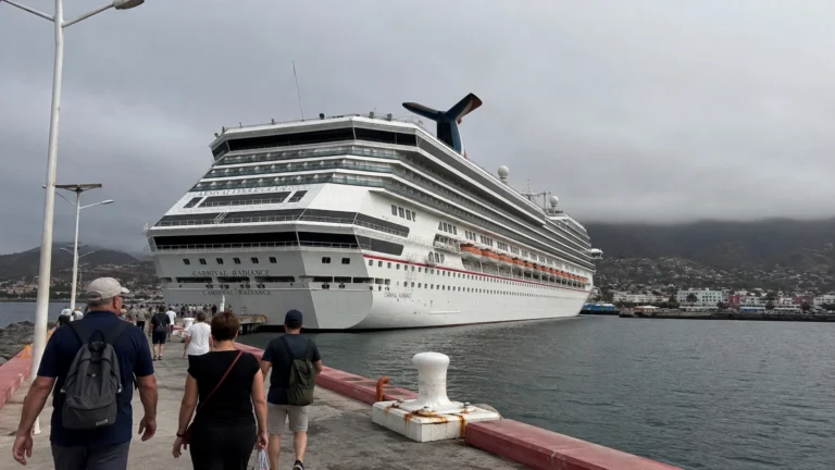 Passengers walking toward a docked Carnival cruise ship beneath cloudy hills