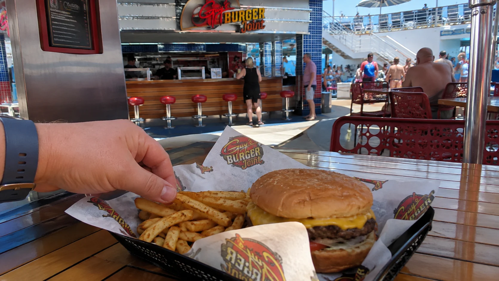 Hand reaching for fries beside a burger from Guy's Burger Joint aboard Carnival Sunrise
