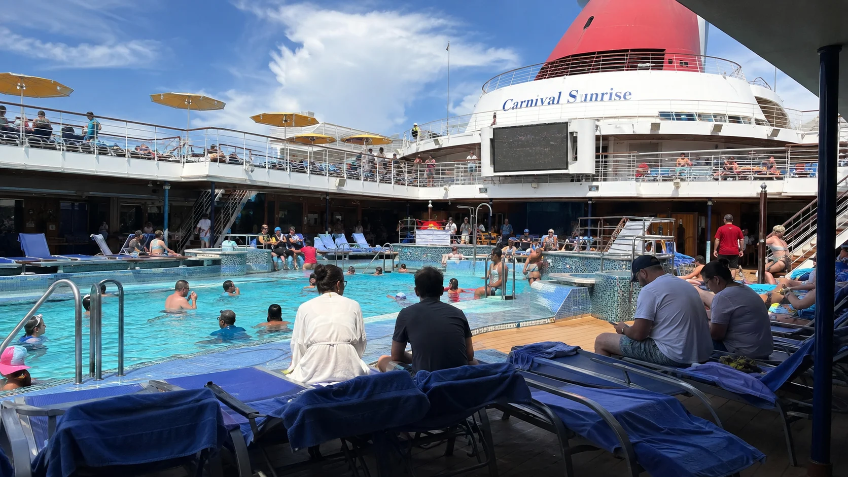 Passengers swimming and relaxing around Carnival Sunrise's outdoor pool