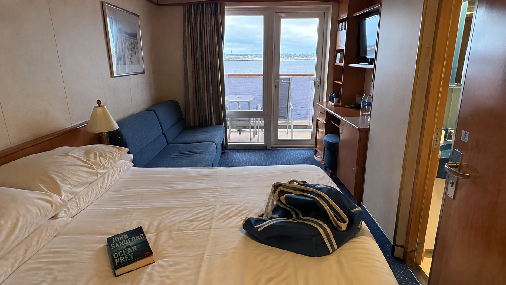 Carnival Valor balcony cabin with a double bed, blue sofa, and ocean view