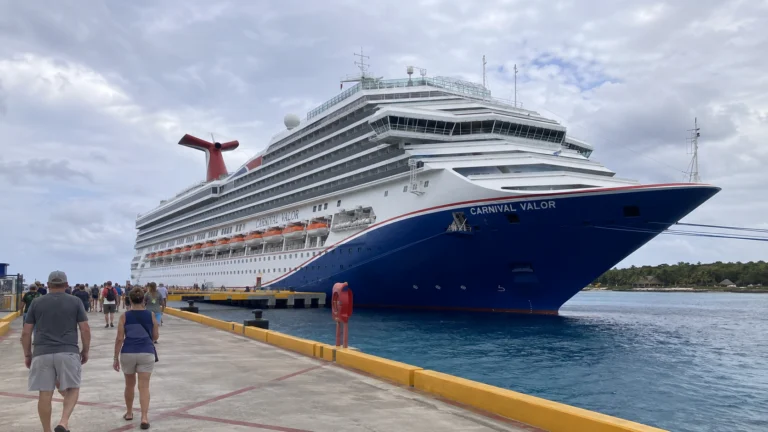 Passengers walking along a pier beside Carnival Valor