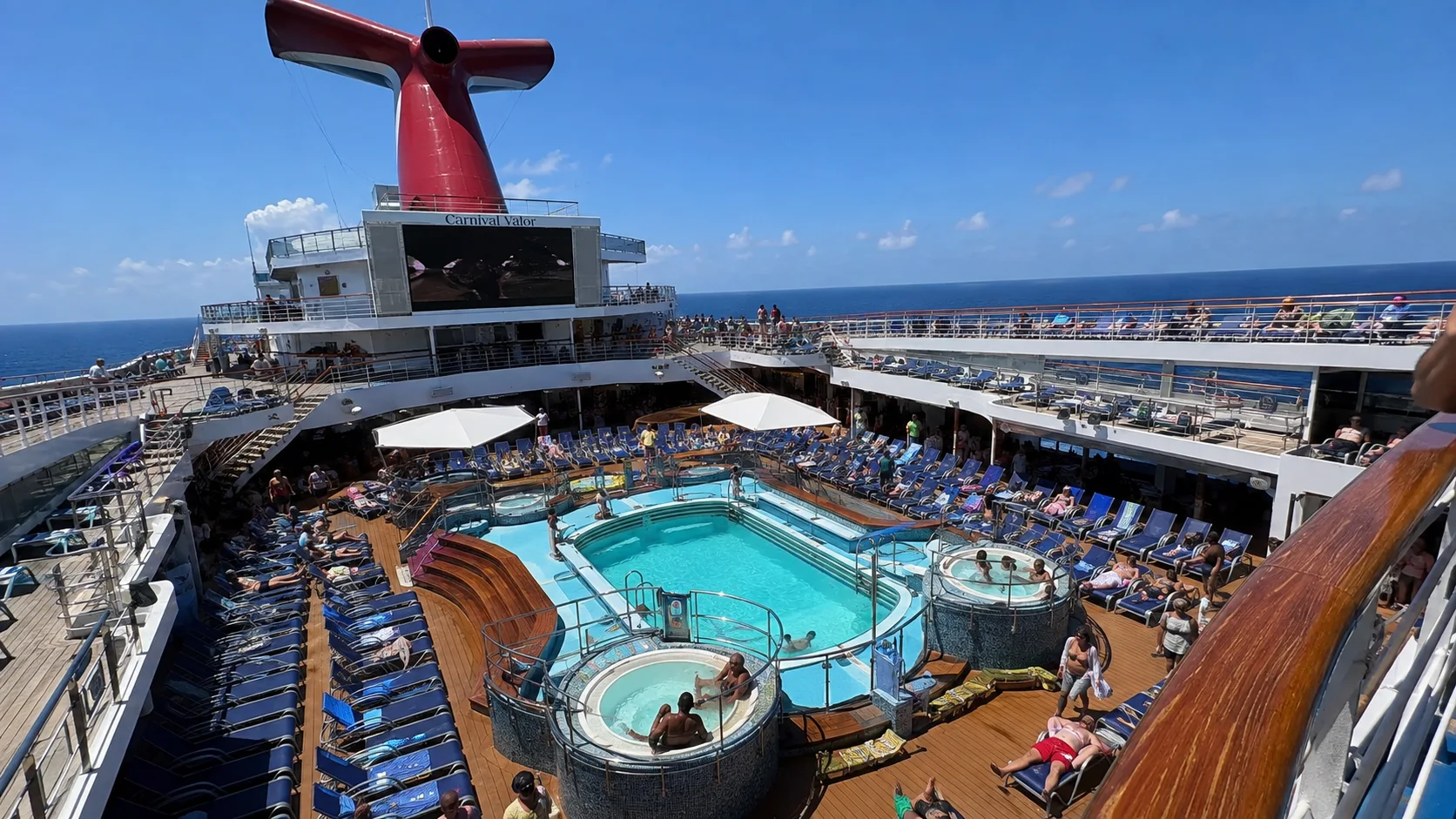 Outdoor cruise ship pool and hot tubs surrounded by lounge chairs