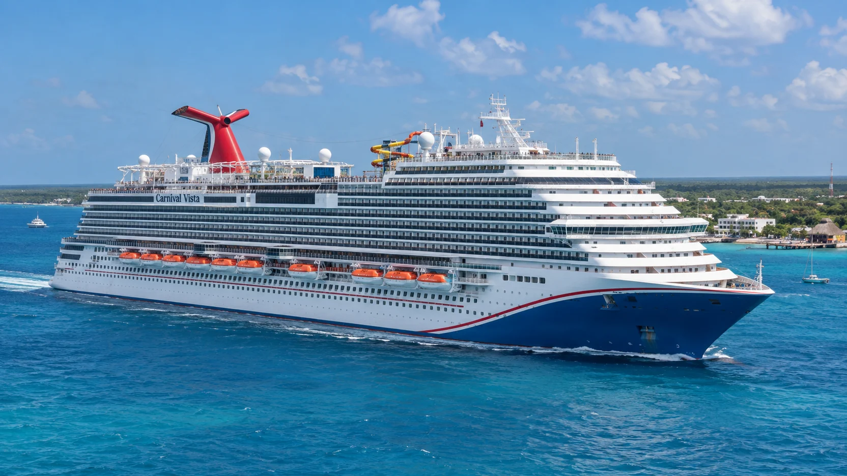 Carnival Vista sails through clear turquoise water near Cozumel, showing its white superstructure, blue-and-red hull and red whale-tail funnel.