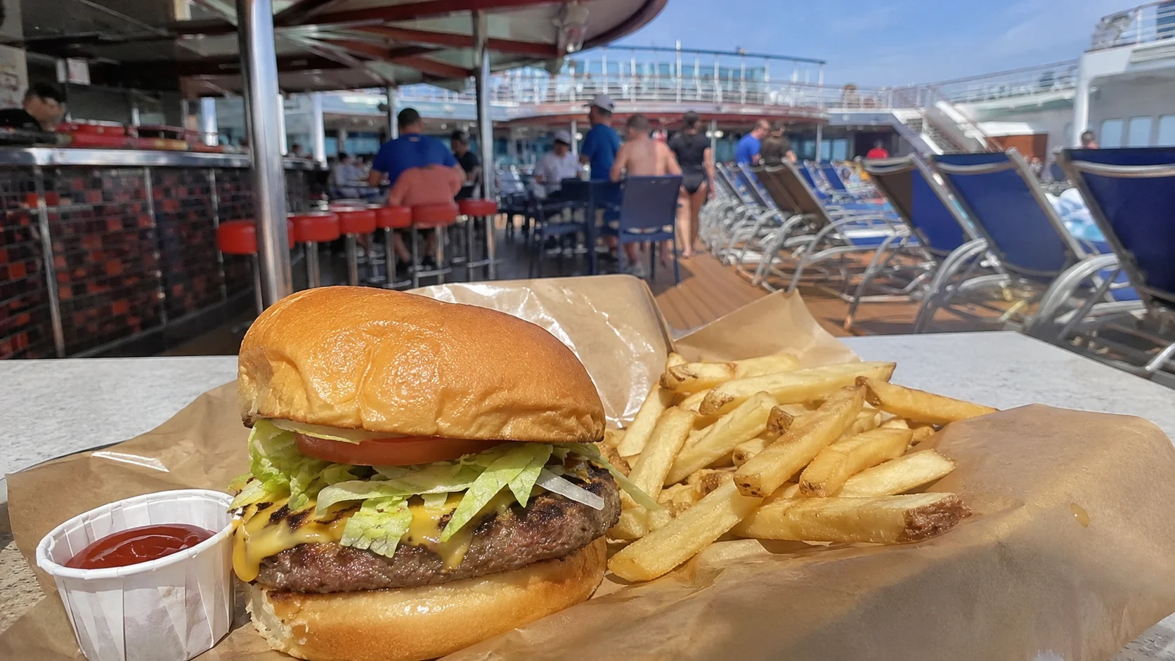 Burger and fries on a table beside cruise ship lounge chairs