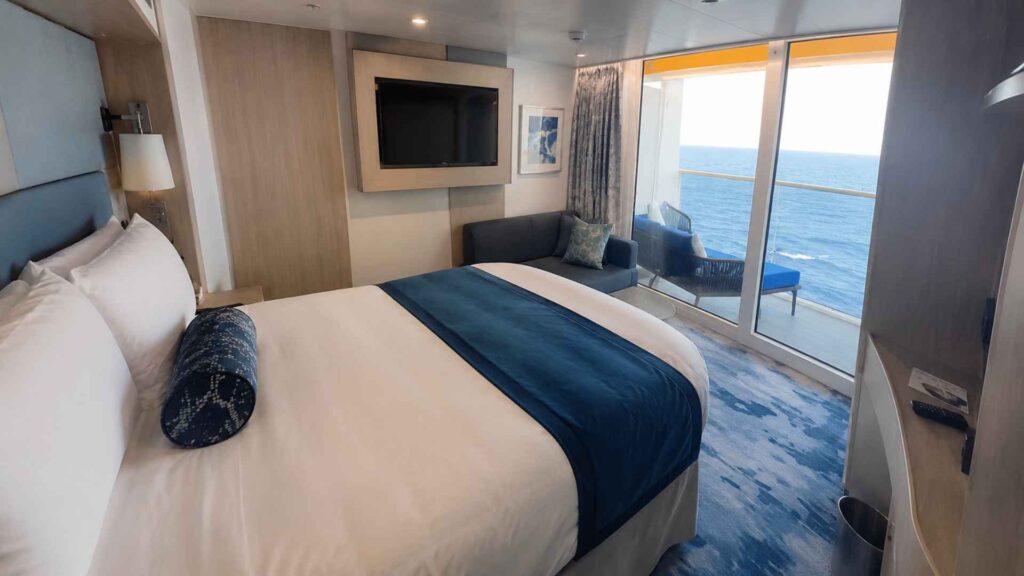 Balcony cabin on Star of the Seas with a wall-mounted television and floor-to-ceiling glass onto the ocean