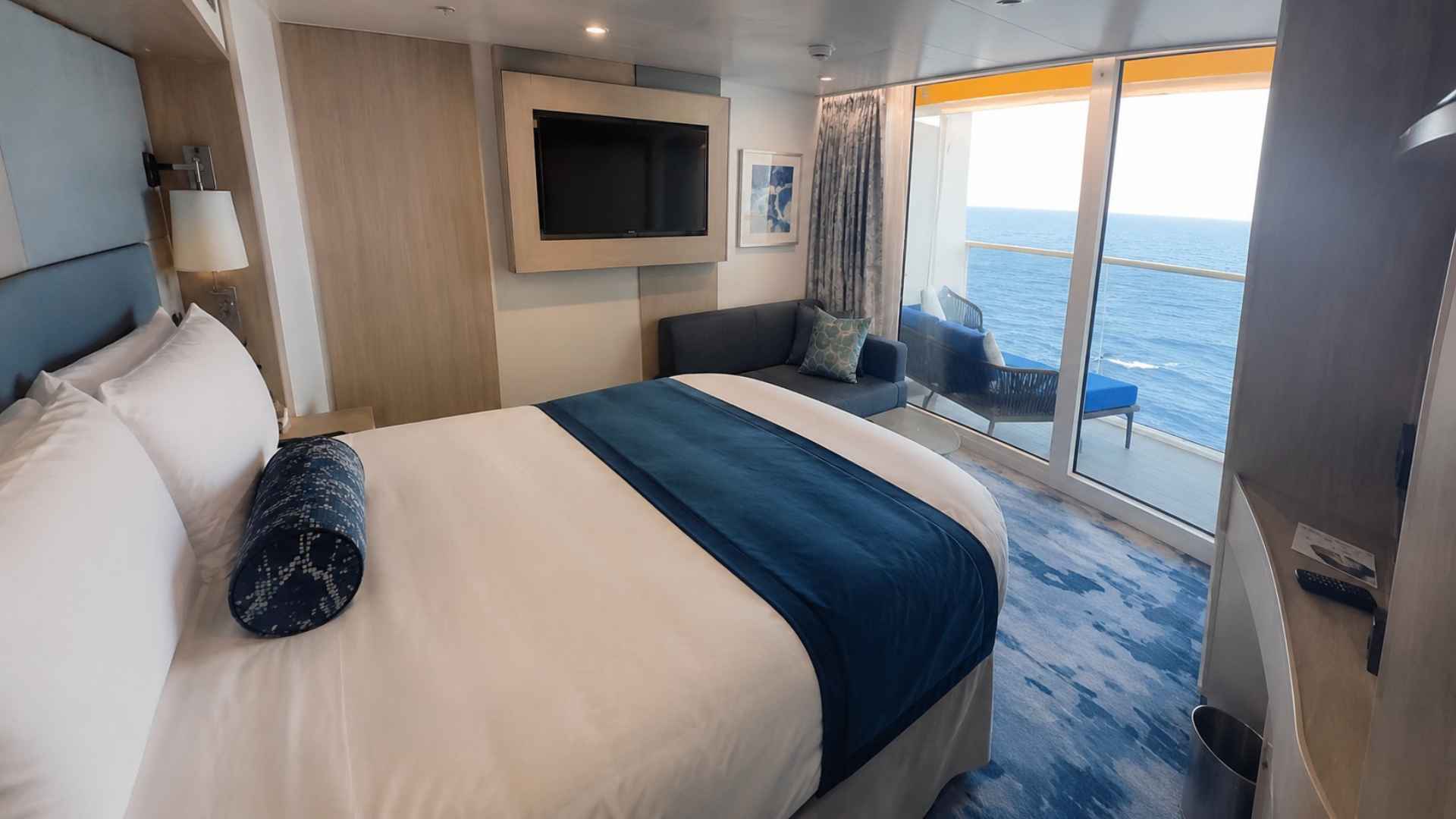 Ocean-facing balcony cabin with a bed, sofa and glass balcony doors