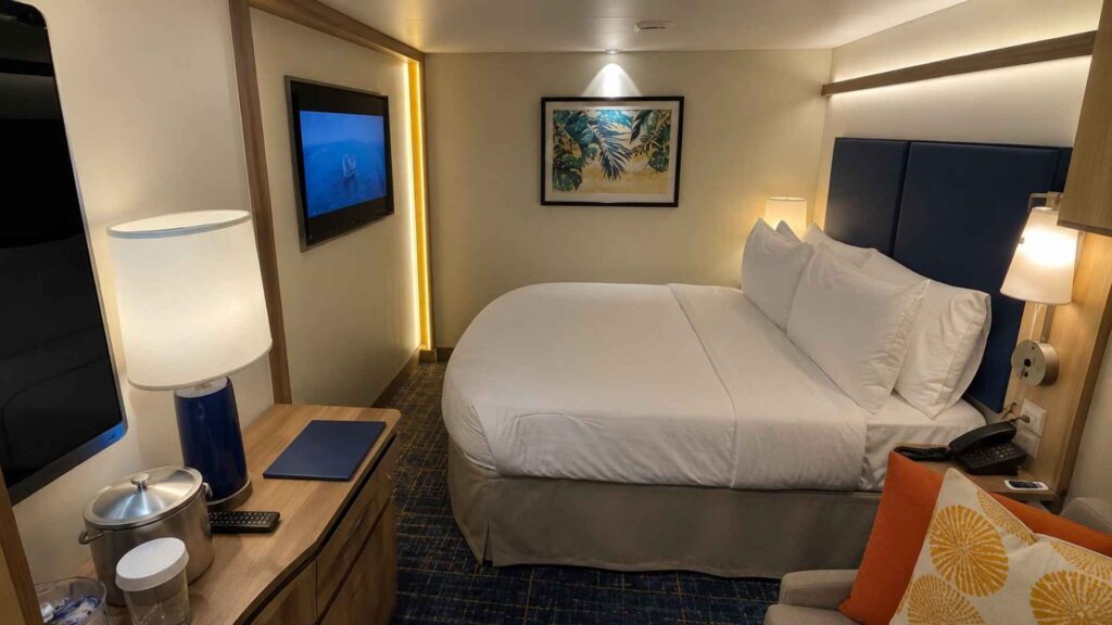 Cabin on Star of the Seas with a bed, desk, table lamp and wall-mounted television