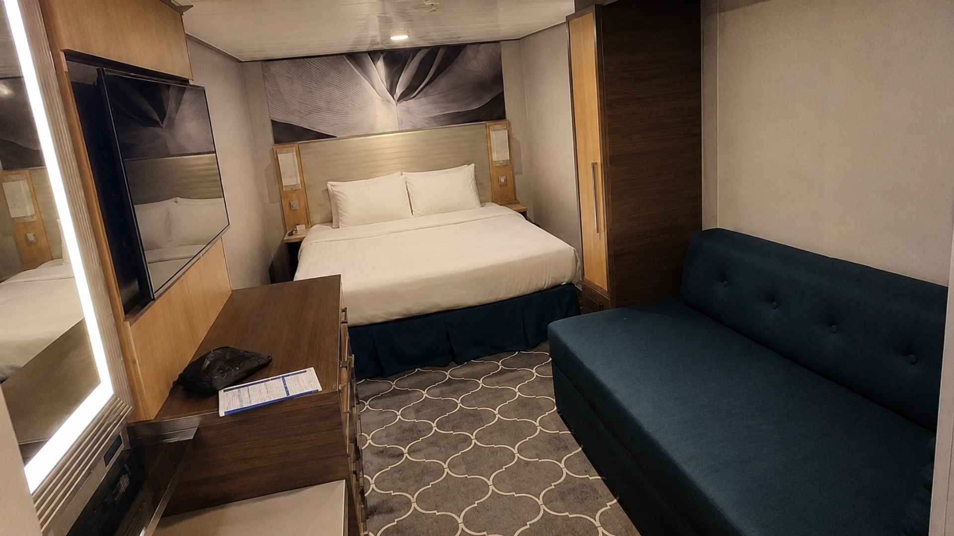Interior cabin on Symphony of the Seas with a bed, teal sofa and a lit headboard panel