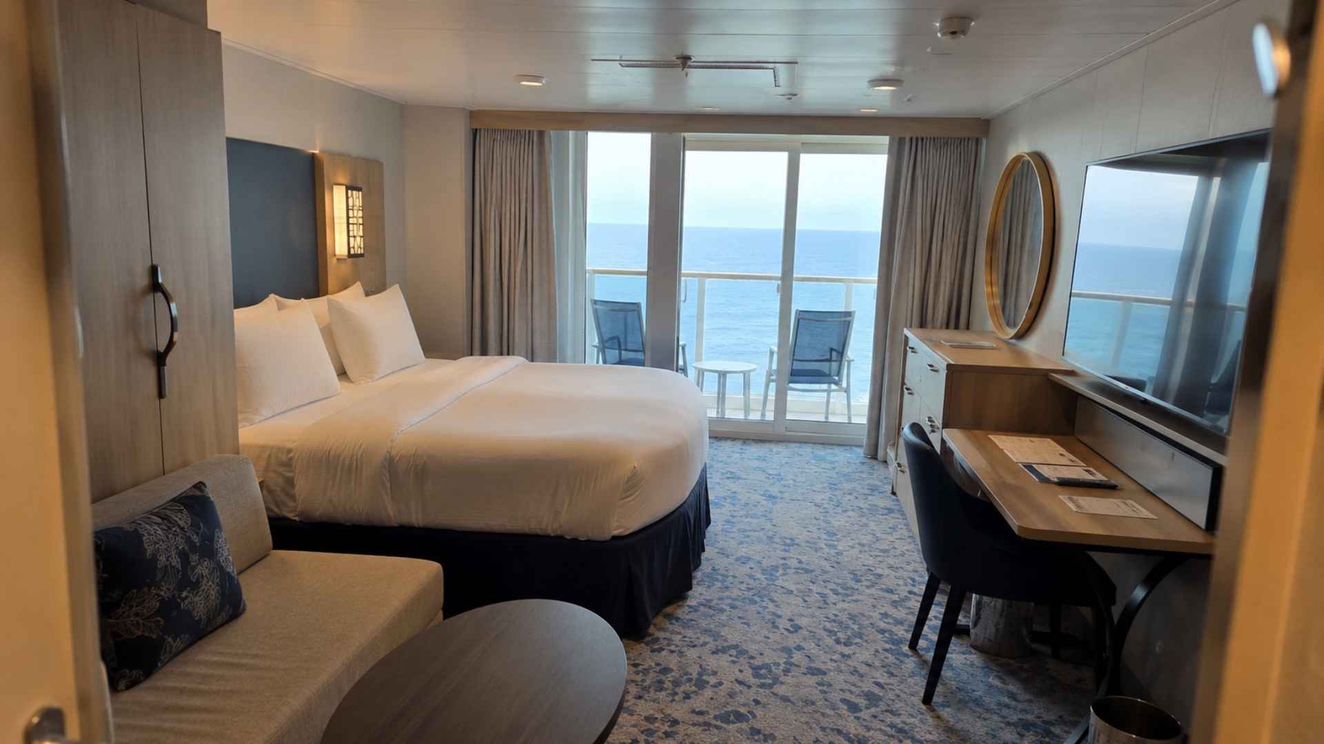 Balcony cabin on Utopia of the Seas with a vanity desk, round mirror and ocean view