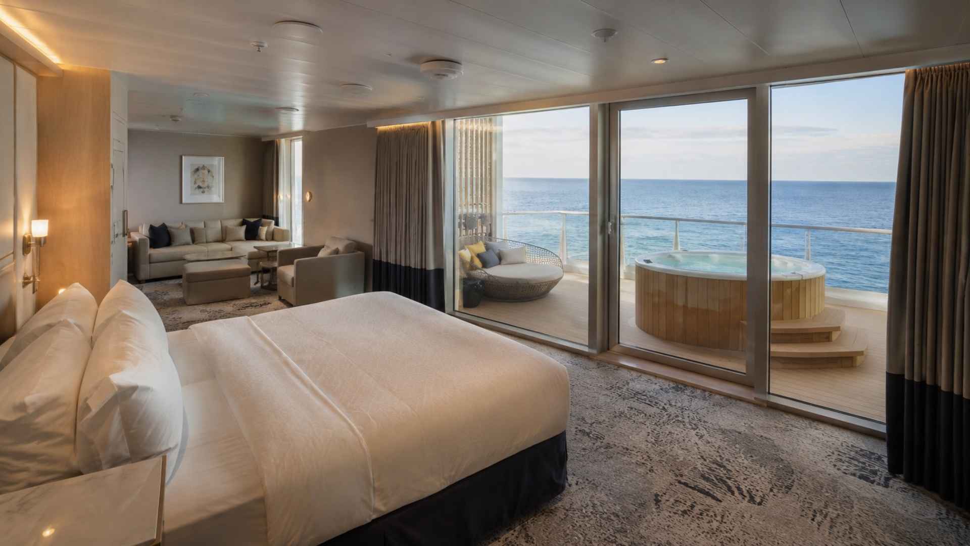 Suite on Utopia of the Seas with floor-to-ceiling glass opening onto a wide balcony with loungers