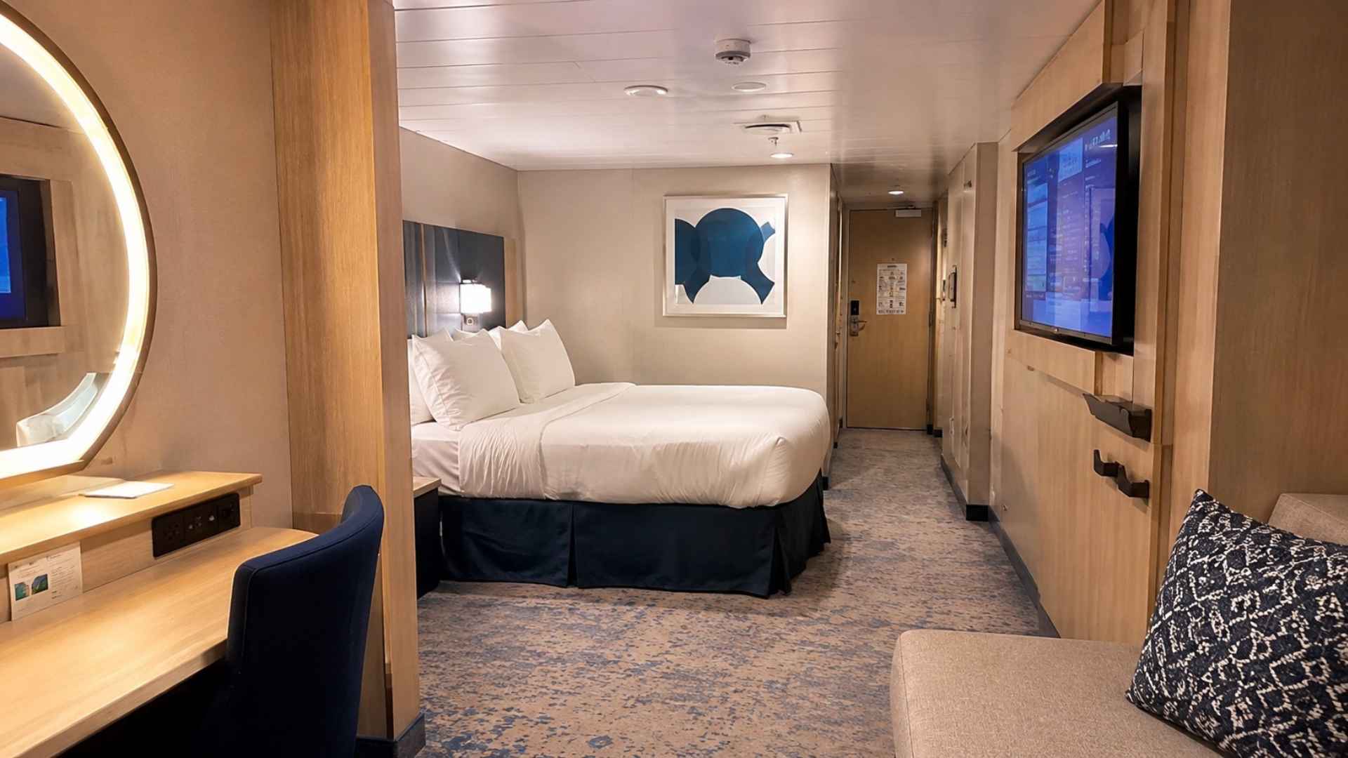 Interior cabin on Utopia of the Seas with a bed, sofa and wall-mounted television